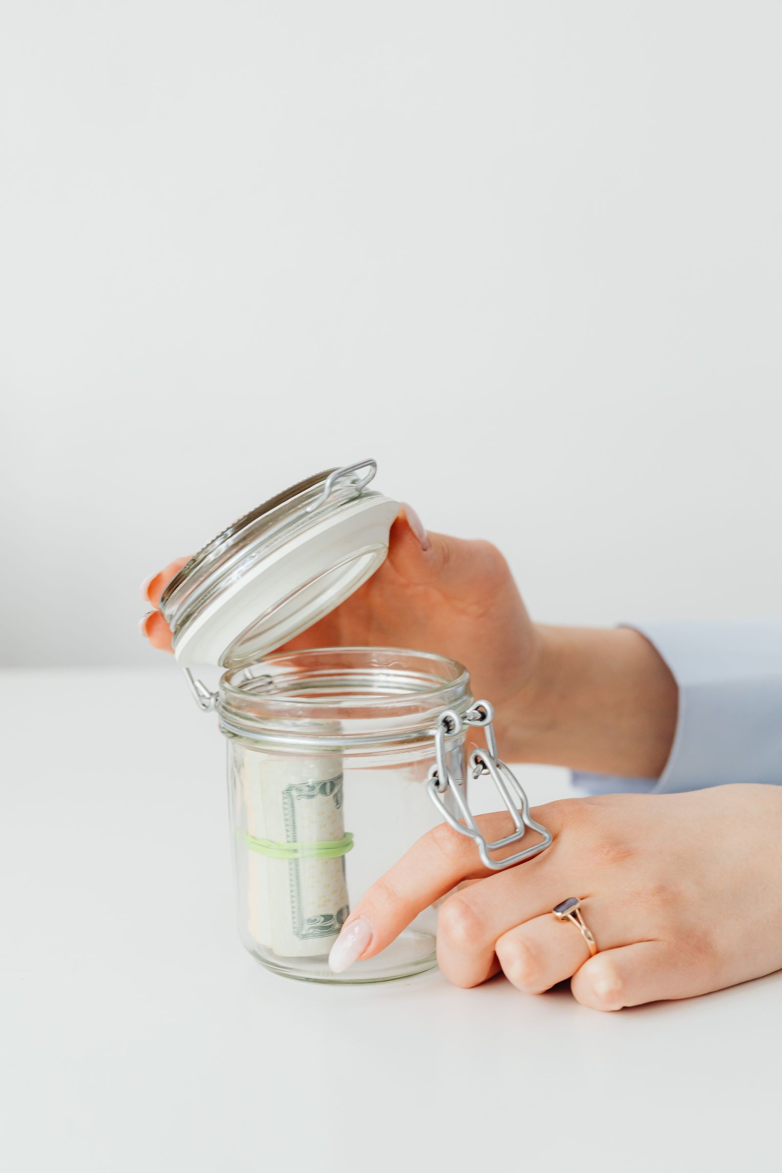 Persona guardando monedas y billetes en un bote de cristal para ahorrar la entrada de una vivienda